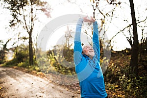 Senior runner doing stretching in sunny autumn nature.