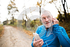 Senior runner in nature with smart phone with earphones.