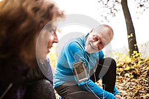 Senior runners in nature, tying shoelaces. Man with smartphone.