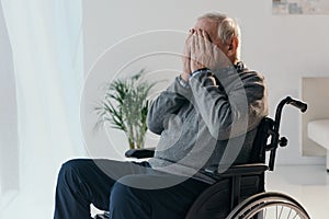 Senior sad man in wheelchair covering his face