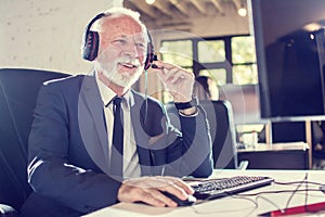 Senior sales agent with headset working on computer in office.
