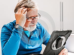 senior seated man looks worriedly at the tablet at home