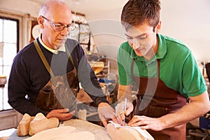 Senior shoemaker training apprentice to make shoe lasts