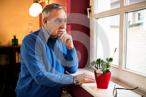Senior sick old man looking through window,staying alone at home