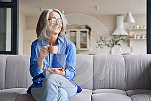 Senior smiling 60s woman portrait at home looking away with cup of tea, coffee.