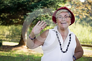 Senior smiling lady with red hat and eyeglasses waving