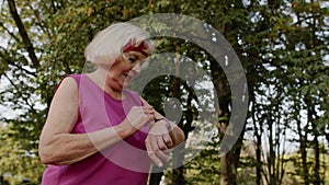 Senior sport runner woman using smart watch, tapping touchscreen, tracking result. Fitness workout