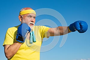 Senior sportive man in boxing stance doing exercises with boxing gloves. Elderly man hitting punching bag. Senior men