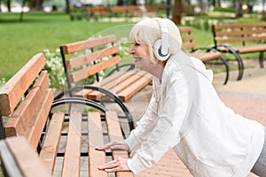 senior sportive woman in headphones training near benches