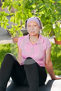 Senior sportive woman sitting on mat sunny