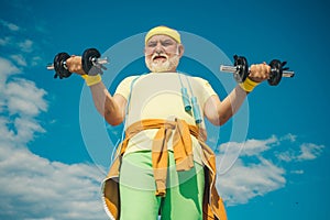 Senior sportman exercising with lifting dumbbell on blue sky background. Isolated, copy space. Senior man in gym working