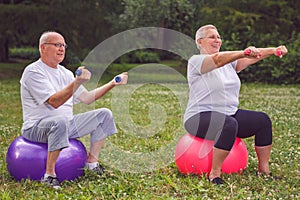 Senior sports couple sitting on fitness ball with dumbbells