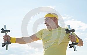 Senior sportsman in sport center. Lifting dumbbells. Body care and healthcare. Senior man exercising on blue sky