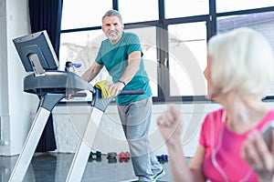 Senior sportsman training on treadmill, senior sportswoman on foreground