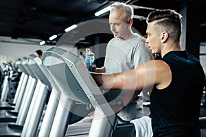 senior sportsman training on treadmill with trainer in gym