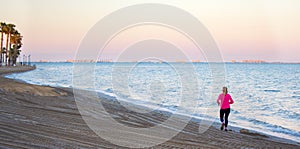 Senior sportswoman running at the beach in Spanish coasts. Athletic old woman practices physical activity, works out, training in