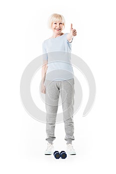 Senior sportswoman showing thumb up gesture and dumbbells on floor