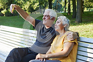 Senior spouses take selfie picture sit on bench in summer park