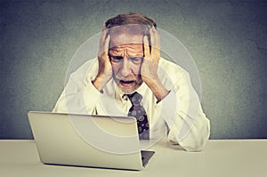 Senior stressed man working on laptop sitting at table