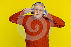 Senior stylish old man listening music via headphones and dancing, happy grandfather pensioner