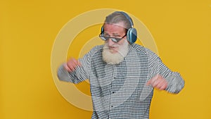 Senior stylish old man listening music via headphones and dancing, happy grandfather pensioner