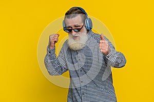 Senior stylish old man listening music via headphones and dancing, happy grandfather pensioner