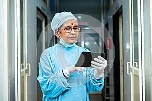 Senior surgeon in operation gown busy checking patient report at hospital corridor o tablet - concept of technology