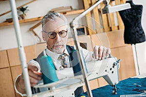 senior tailor touching spool of thread on sewing machine
