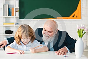 Senior teacher or grandfather and school boy pupil in classroom at school. Elementary pupil reading and writing with