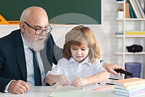 Senior teacher or grandfather and school boy pupil in classroom at school. Private lesson. Old tutor teacher help little