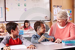 Senior teacher sitting with elementary school kids in class