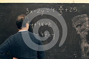 Senior teacher writing equations on a blackboard in a classroom