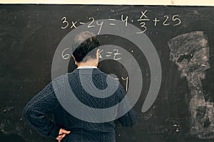 Senior teacher writing equations on a blackboard in a classroom