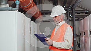 Senior technician writing on clipboard while checking batch of made fridges