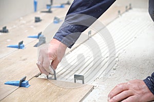 Worker hands laying ceramic wood effect tiles using tile levelers.
