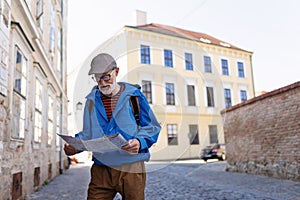 Senior tourist exploring new city, interesting places. Elderly man holding paper map, looking for the route. Solo