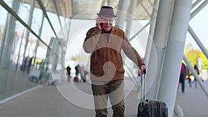 Senior tourist grandfather man walking on international airport hall using mobile phone conversation