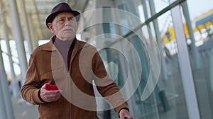 Senior tourist grandfather man walking on international airport hall, using mobile phone, texting