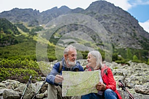 Senior tourists sitting on rocks and looking at the route on a map.