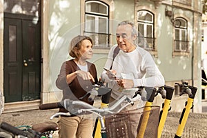 Senior Travelers Couple Using Smartphone Renting Electric Scooters Outdoor