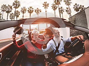 Senior trendy couple inside a convertible car on holiday time - Mature people having fun doing a road trip during summer vacation