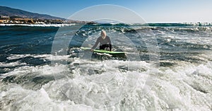 Senior trying to surf a wave on the sea at the beach alone with black wetsuit and green surftable - vacation at the sea and active