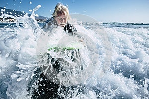 Senior trying to surf a wave on the sea at the beach alone with black wetsuit and green surftable - vacation at the sea and active