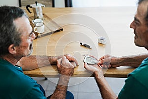 Senior twin men making blood glycemia test for diabetes check - Focus on hand holding glucometer