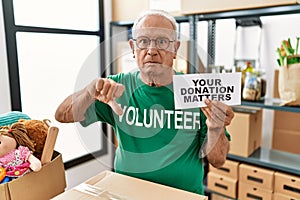 Senior volunteer man holding your donation matters with angry face, negative sign showing dislike with thumbs down, rejection