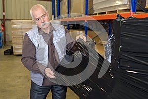 Senior warehouse worker covering pallet goods in black shrinkwrap