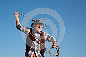 Senior western cowboy throwing lasso rope. Bearded wild west man with brown jacket and hat catching horse or cow. Rodeo
