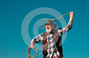 Senior western cowboy throwing lasso rope. Bearded wild west man with brown jacket and hat catching horse or cow. Rodeo