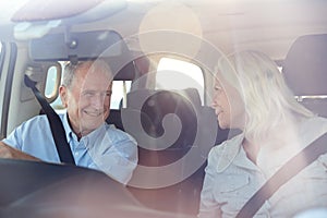 Senior white couple driving in their car smiling to each other, seen through front windscreen