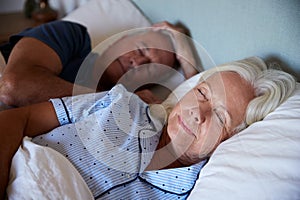 Senior white couple lying asleep in their bed, waist up, close up